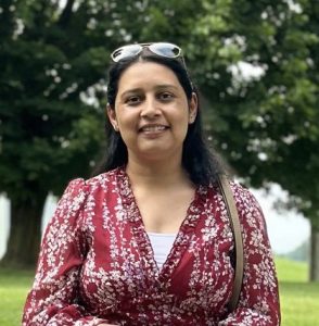 Smiling woman with long dark hair wearing a red dress and standing in a park
